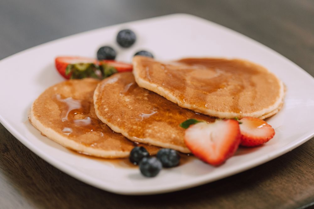 Three golden Oat-EH oat pancakes with maple syrup, strawberries and blueberries